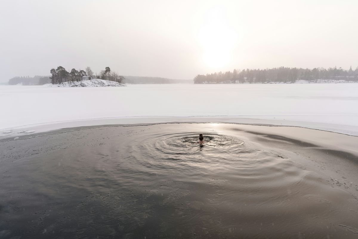 A person taking an avanto ice plunge in a Finnish winter lake surrounded by snow