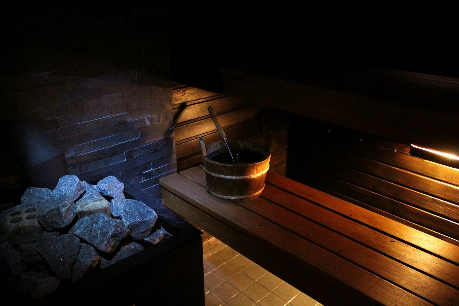 Wood-fired Finnish sauna interior with kiuas stones and a wooden bucket